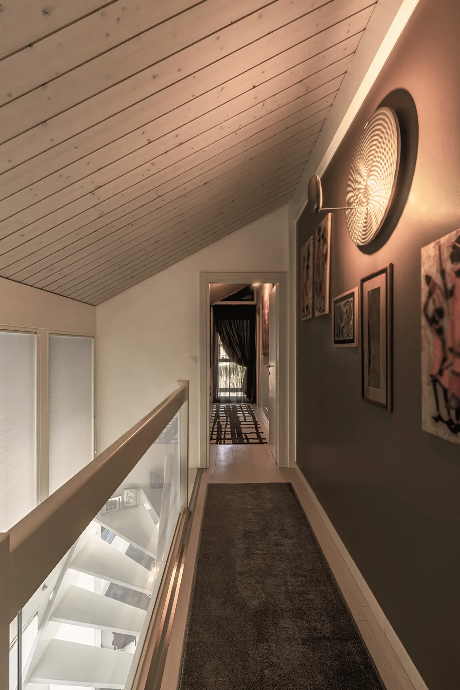 Photo de l'escalier et du couloir du premier étage avec les détails du mur peint dans les tons de gris tourterelle, du plafonnier Artemide, de la moquette grise et du parquet clair ; rénovation par le studio Elles Interior Design.
