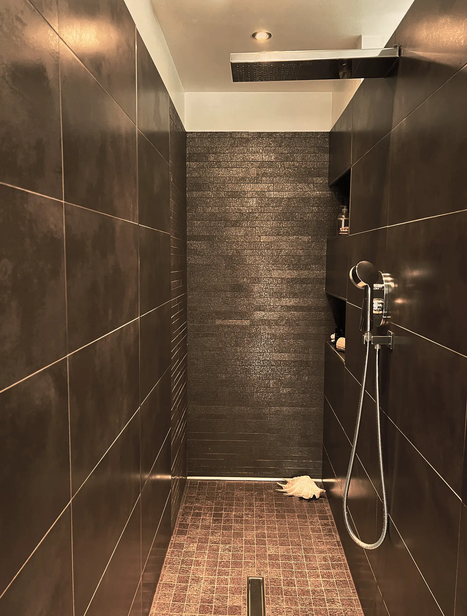 Photo de la douche avec son sol en céramique brune et les revêtements muraux en 3 calepinages différents ; rénovation par le studio Elles Interior Design.