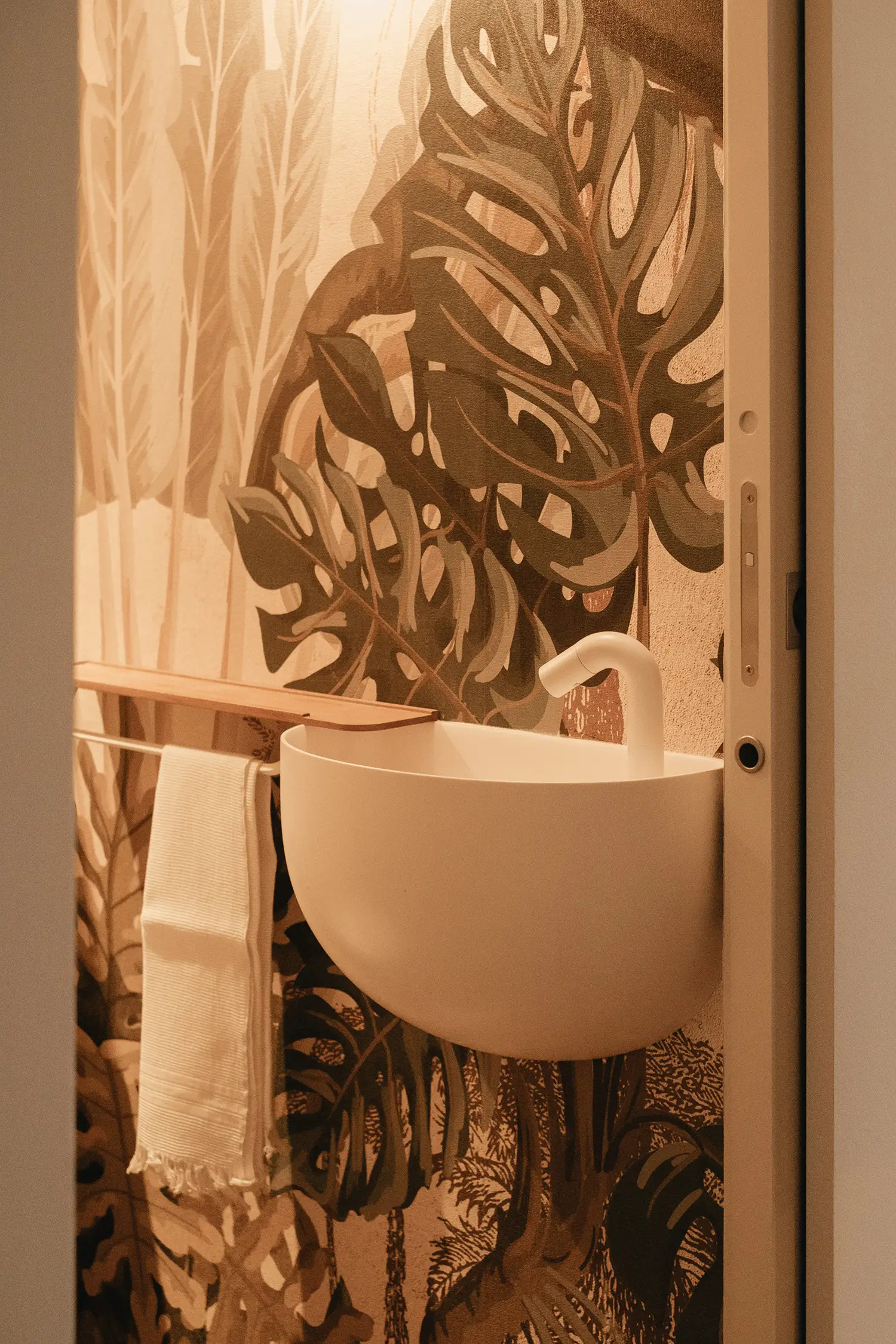 Photo du lave main dans les toilettes avec porte rétractable, ambiance écolo en faisant entrer un jardin tropical dans la pièce en suivant l'un des différents principes de la biophilie ; projet de rénovation par le studio Elles Interior Design.
